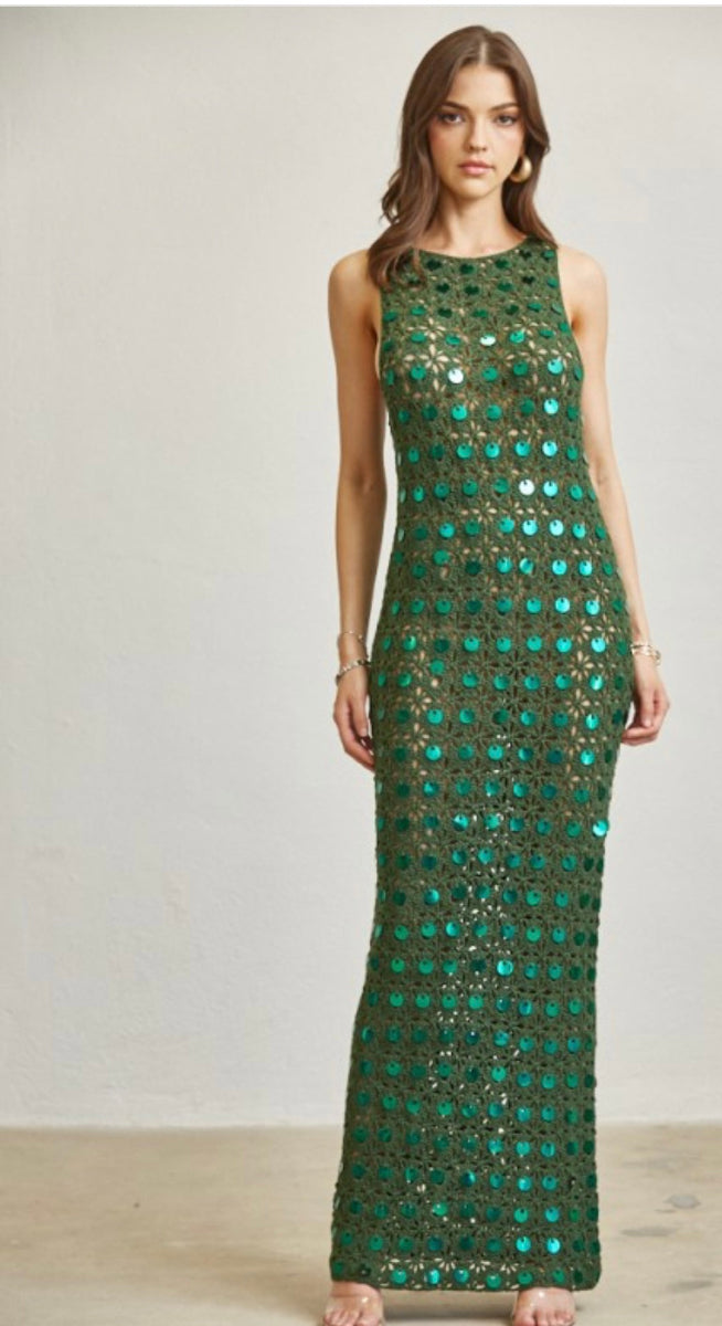 Woman wearing a green crochet with sequin dress against a plain background