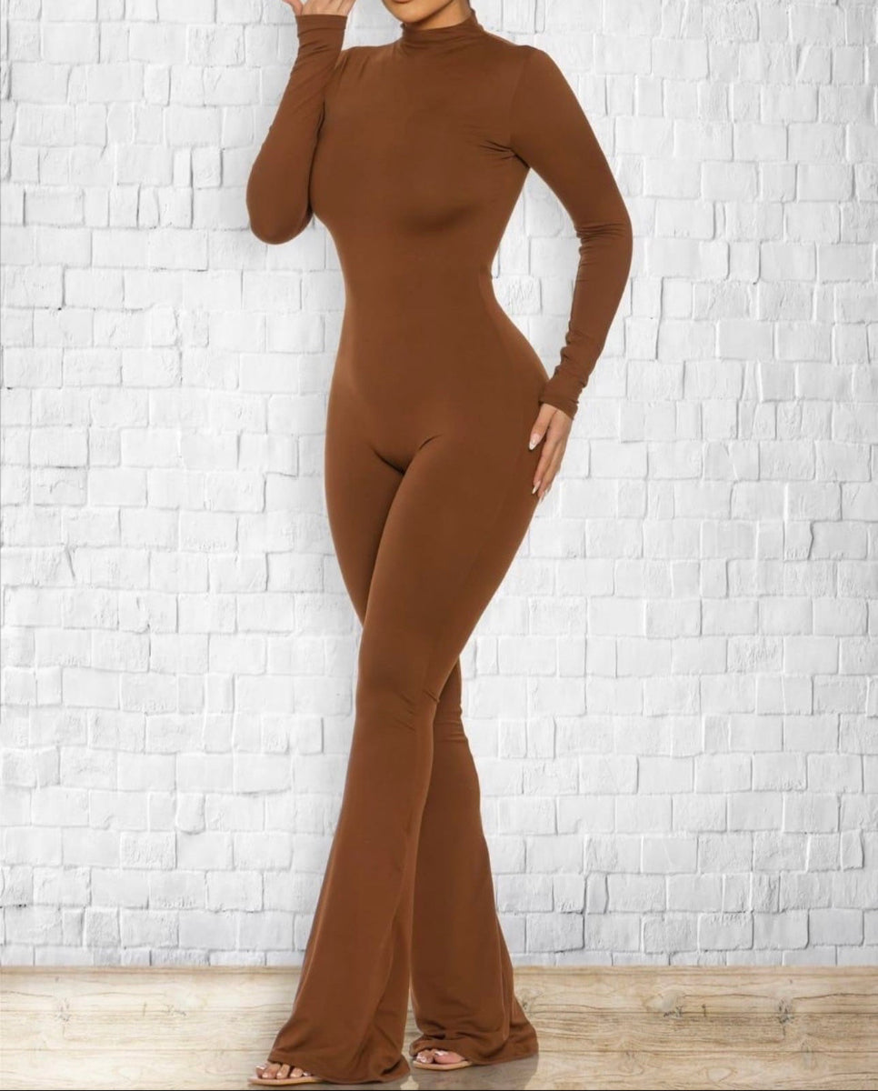 Woman wearing a brown bodysuit against a white brick wall.