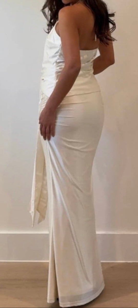 Woman wearing a white evening gown with a high slit on a plain background