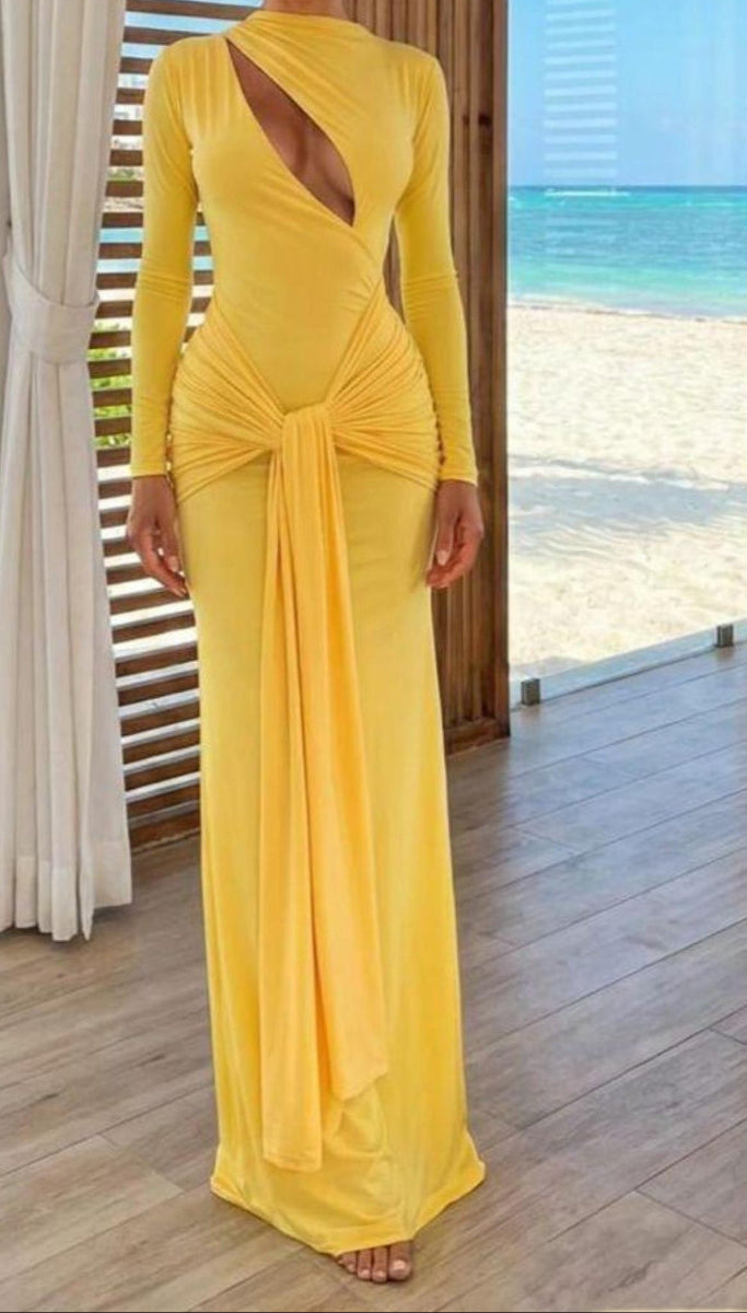 Yellow evening gown with long sleeves and a cut-out back, worn indoors with a window view of the ocean.